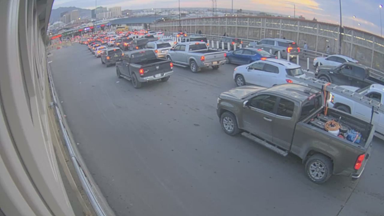 Traffic is slow on a multi-lane highway with numerous trucks and cars in a line, suggesting a congestion point near a checkpoint or toll area; no visible work zones or incidents.
