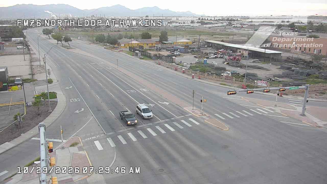 A wide, multi-lane highway intersection with light traffic, featuring a silver SUV and a dark pickup truck approaching the crosswalk under clear skies; no visible work zones or incidents.