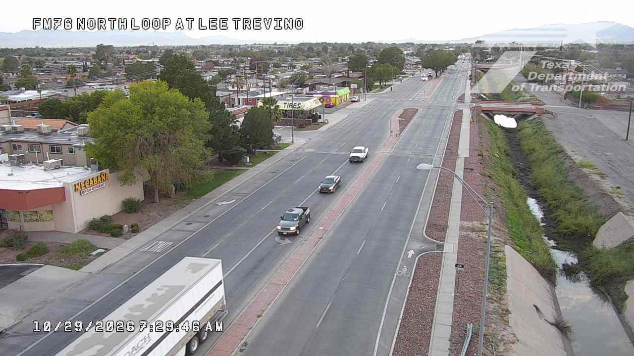Light traffic on a multi-lane road with a semi-truck, pickup trucks, and a sedan moving in separate lanes; no visible work zones or incidents; dry conditions with distant mountains in the background.