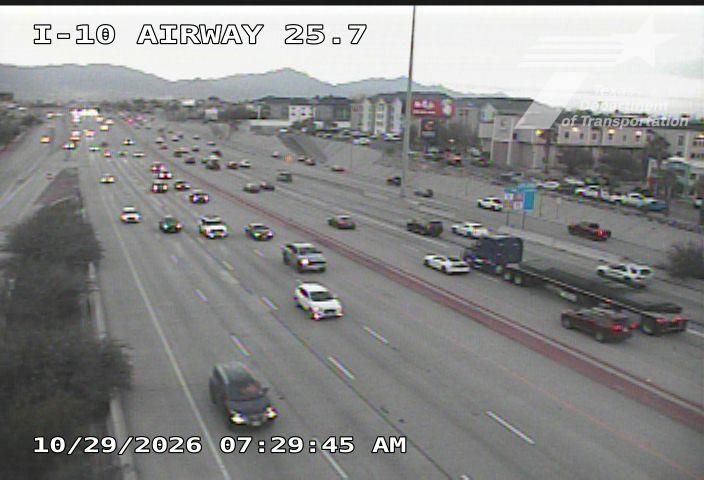 Multi-lane highway with moderate traffic flow, including a large semi-truck and several cars moving in both directions under overcast skies.