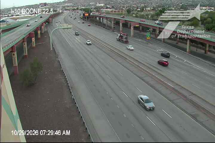 Multi-lane highway with moderate traffic flow under overpasses, featuring a semi-truck and several passenger vehicles moving freely.