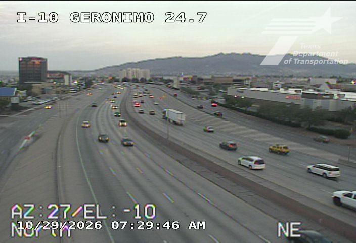 Multi-lane highway with moderate traffic flow, vehicles including cars and a semi-truck, under clear sky with distant hills in background.