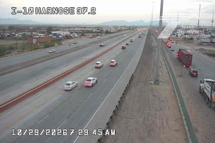 Highway traffic flows smoothly with light vehicle movement, while a line of trucks and vehicles waits at a construction zone on the right side of the road.