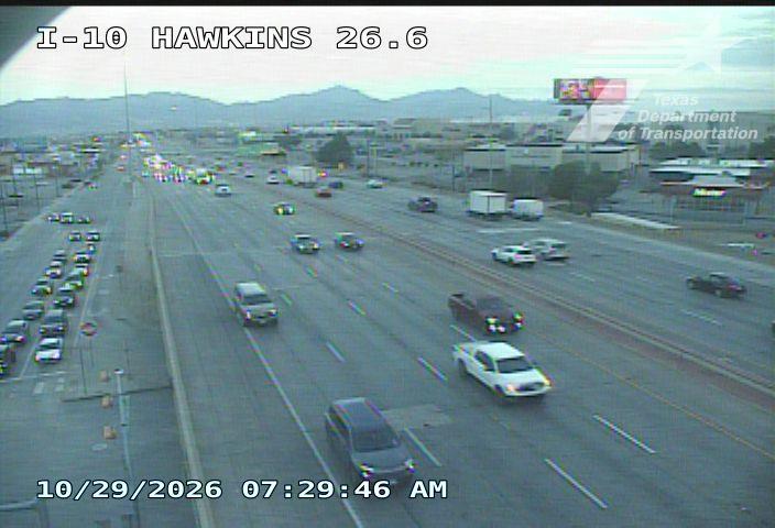 Multi-lane highway with moderate traffic flow, vehicles moving in both directions under clear skies with distant mountains in view.