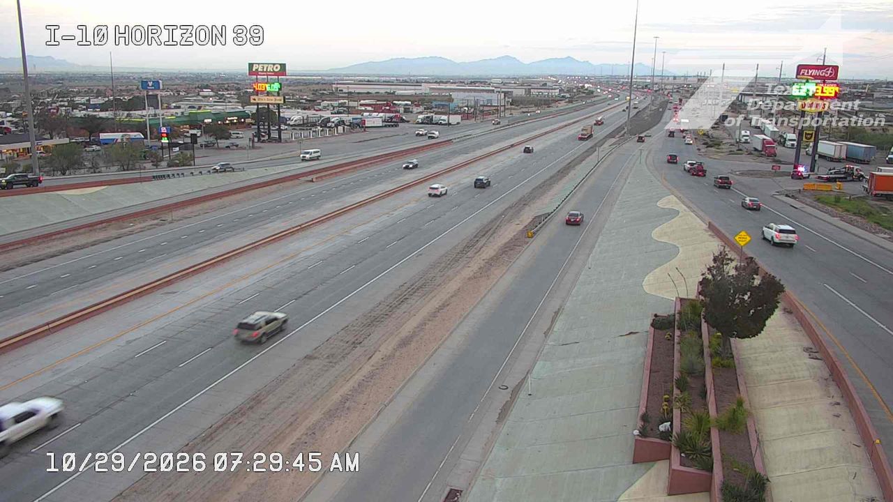 Multi-lane highway with moderate traffic flowing in both directions, featuring commercial signage and distant mountains under clear skies.