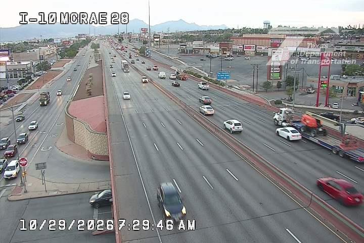 Multi-lane highway with moderate traffic flow, including a large flatbed truck hauling heavy equipment and several cars moving freely across lanes.