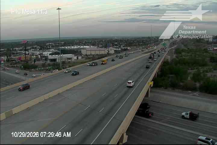Multi-lane highway with moderate traffic flow under clear skies, featuring vehicles moving freely across an overpass and adjacent roadways.