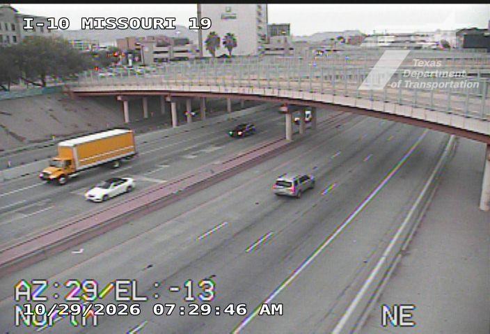 Multi-lane highway with moderate traffic flow under an overpass, featuring a yellow semi-truck, a white sedan, and a silver SUV moving in the same direction.