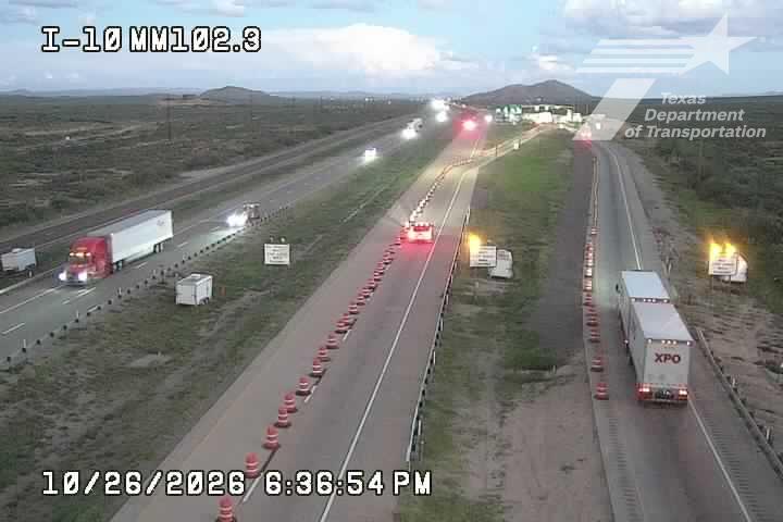 Highway with multiple lanes of traffic moving freely, featuring semi trucks and a work zone with cones and barriers; weather appears clear with good visibility.