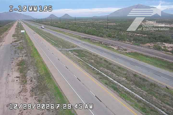 A wide, multi-lane highway stretches through a desert landscape with distant mountains, showing light traffic with a few vehicles moving freely.