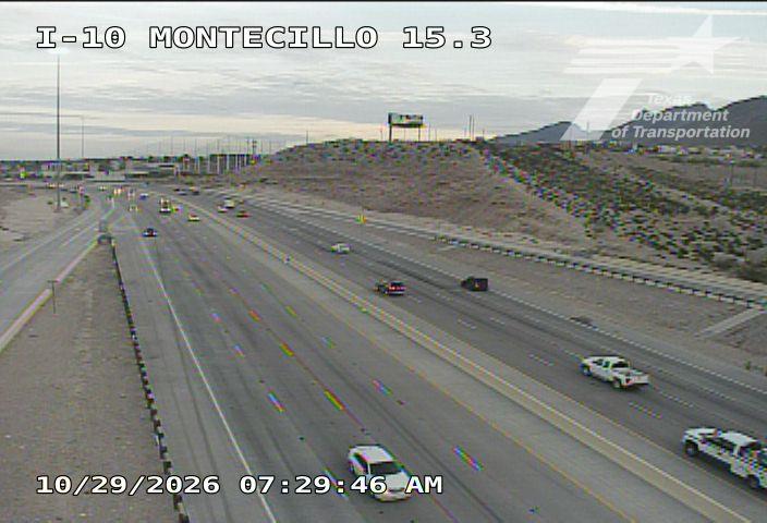 Light traffic flows on a multi-lane highway with scattered vehicles, including a white pickup truck and a police vehicle, under an overcast sky.
