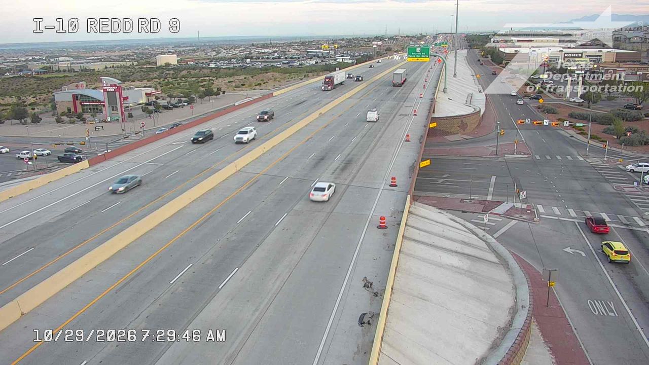 Light traffic flows on a multi-lane highway with vehicles moving at moderate speeds; no visible incidents or road work, and a few cars are stopped at an intersection.