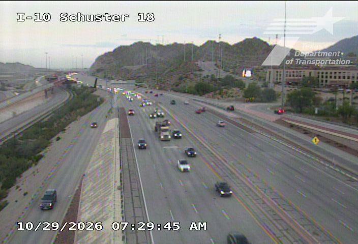 Multi-lane highway with moderate traffic flow, vehicles moving in both directions under clear skies with distant hills in the background.