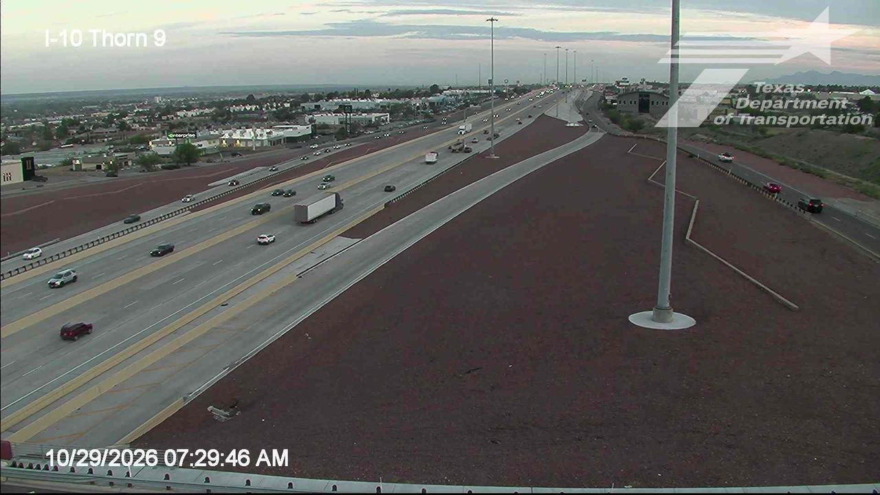 Light traffic flows along a multi-lane highway with a large truck and several cars moving in both directions; no visible work zones or incidents, under clear skies with good visibility.
