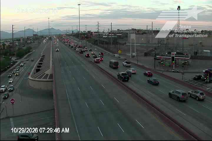 Multi-lane highway with moderate traffic flow, featuring a bridge overpass and distant mountains under clear skies.