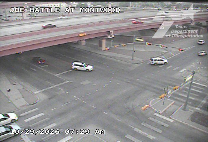 Vehicles navigate a multi-level intersection under an overpass with moderate traffic flow; no visible incidents or road work.