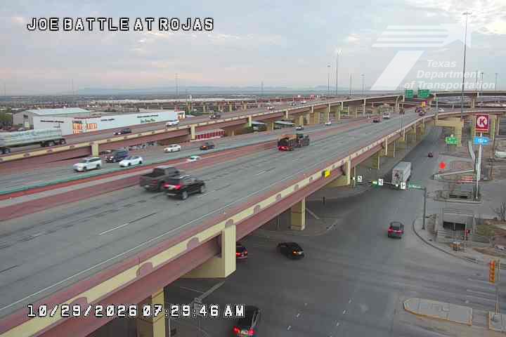 Multi-level highway with moderate traffic flow under clear skies, featuring vehicles moving freely across elevated lanes and a lower intersection with turning cars.