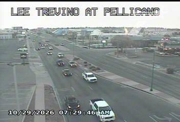 Light traffic flows through a multi-lane intersection with several vehicles, including trucks and cars, moving in both directions under clear skies.