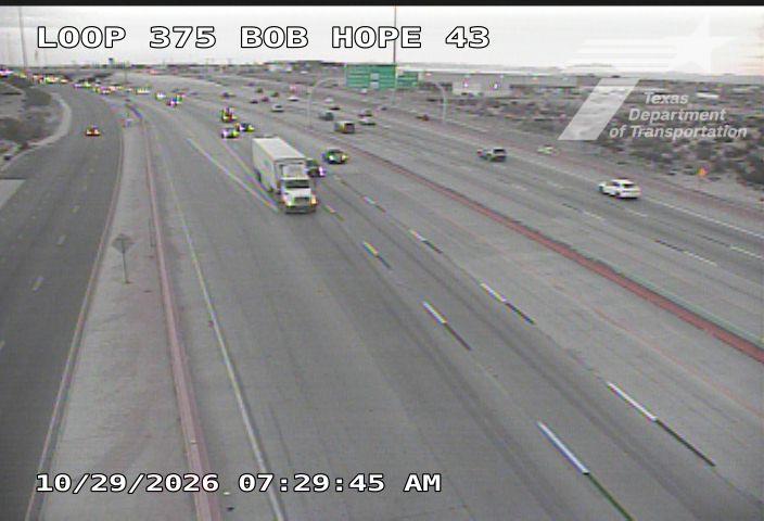 Multi-lane highway with moderate traffic flow, featuring a white semi-truck and several cars moving in both directions under overcast skies.