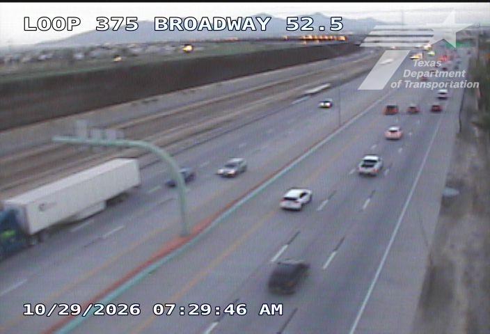 Multi-lane highway with moderate traffic flow, including a semi-truck and several passenger vehicles moving in both directions under clear sky conditions.