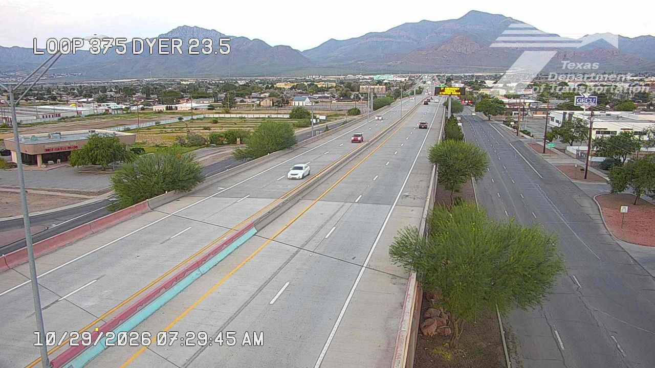 Light traffic flows on a multi-lane highway with distant mountains in the background under clear skies.