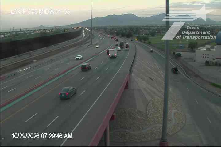 Light traffic flows on a multi-lane highway with vehicles moving at moderate speeds, including cars and a white truck, under clear skies with distant mountains in view.