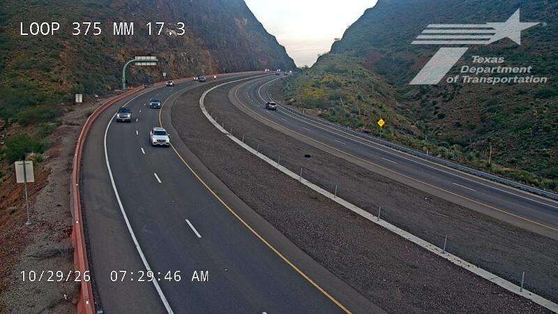 A multi-lane highway curves through a mountainous landscape with light traffic moving in both directions; no visible incidents or road work.
