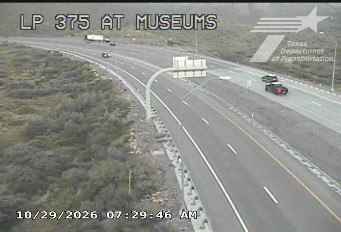 Light traffic on a multi-lane highway with a few vehicles moving steadily, surrounded by dry vegetation and hills under clear conditions.