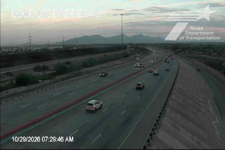 Light traffic flows along a multi-lane highway with distant mountains under a clear sky.
