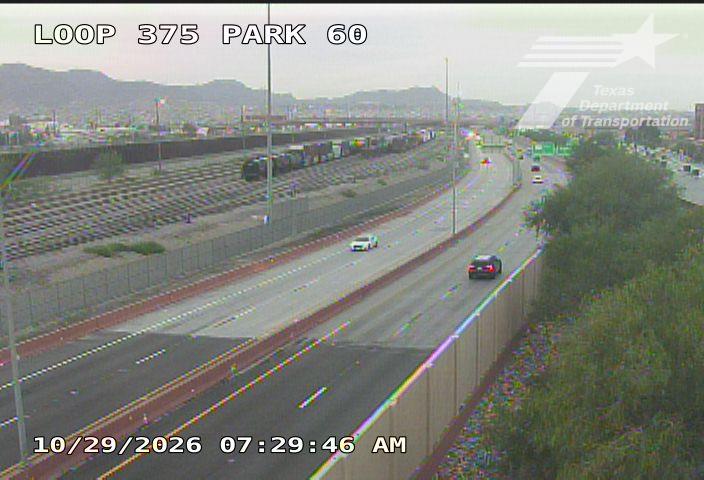 Light traffic flows on a multi-lane highway with a few vehicles visible, bordered by a concrete barrier and greenery; no work zones or incidents are present.