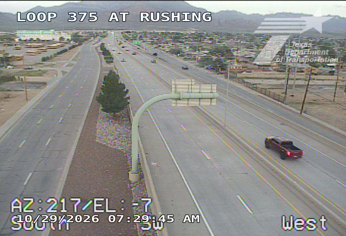 A multi-lane highway with moderate traffic flows in both directions, featuring a red pickup truck in the right lane and distant vehicles on the opposite side; clear skies and dry pavement indicate good weather conditions.