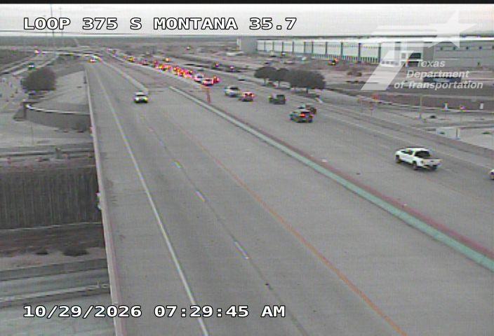 Traffic is slow on a multi-lane highway with a line of vehicles stopped due to an incident ahead, while a white pickup truck and other cars move cautiously through the lanes.