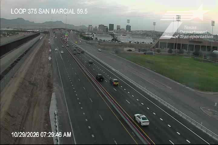 Light traffic flows on a multi-lane highway with a construction zone on the left, under clear skies with distant mountains visible in the background.