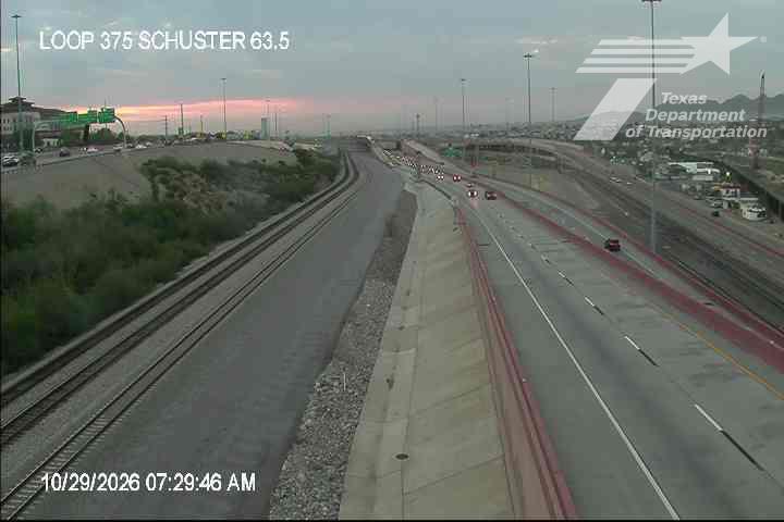 Multi-lane highway with light traffic moving in both directions, adjacent to a set of parallel train tracks under clear, early morning skies.