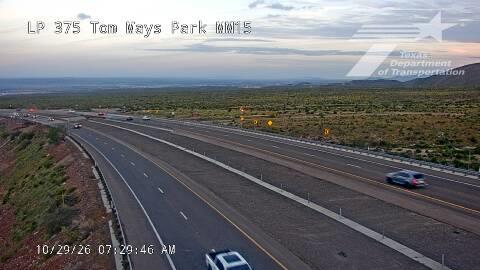 A multi-lane highway stretches through a desert landscape with light traffic moving in both directions under a partly cloudy sky.