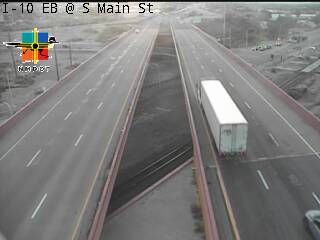 A white semi-truck travels on a multi-lane highway overpass with light traffic; weather appears overcast and dry.