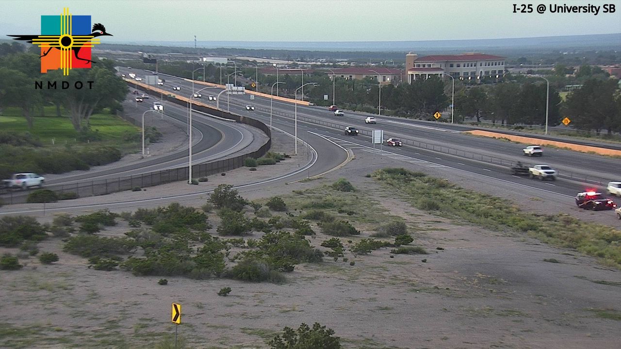 A multi-lane highway curves through a dry, grassy landscape with moderate traffic flow; a crash scene with emergency vehicles is visible on the right side of the road.