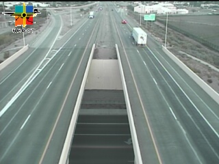 A multi-lane highway with light traffic, featuring a central overpass and a white semi-truck moving in the right lane; weather appears clear and dry.