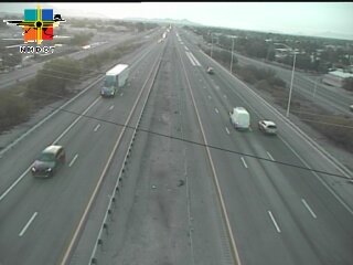 Multi-lane highway with moderate traffic flow, featuring a semi-truck, several passenger vehicles, and a white van traveling in the same direction. Weather appears clear with good visibility.