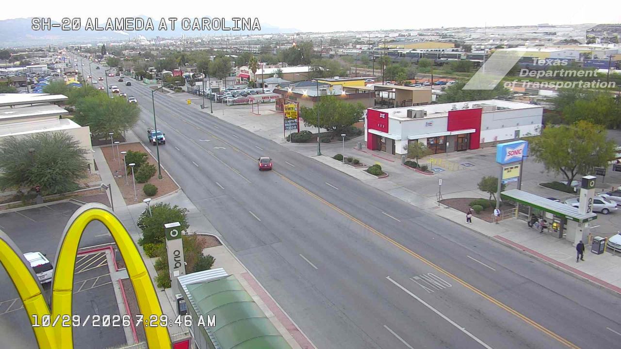 Light traffic flows along a multi-lane urban road with commercial establishments on both sides, including a Sonic and McDonald's, under clear skies.