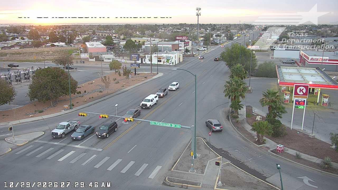 Vehicles are stopped at a traffic light at an intersection with commercial buildings and a gas station nearby; the scene is clear and calm under soft daylight.