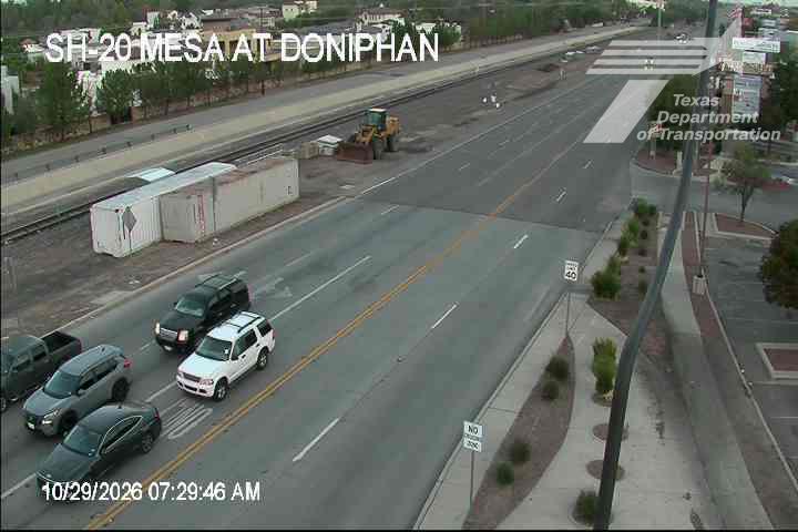 A multi-lane highway with light traffic moving in one direction, featuring a construction zone with a yellow loader and overturned shipping containers; weather appears clear and dry.