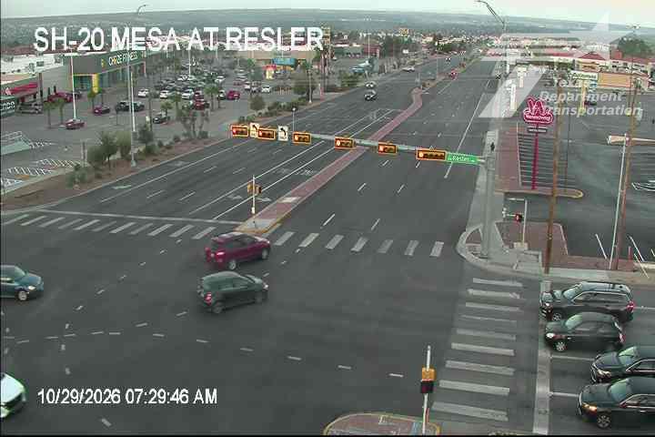 Vehicles navigate a multi-lane intersection with traffic signals, including a red car turning left and a dark sedan crossing the street; no visible incidents or road work.