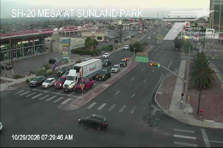 A multi-lane intersection with moderate traffic, including a white semi-truck and several cars, under overcast skies with good visibility.