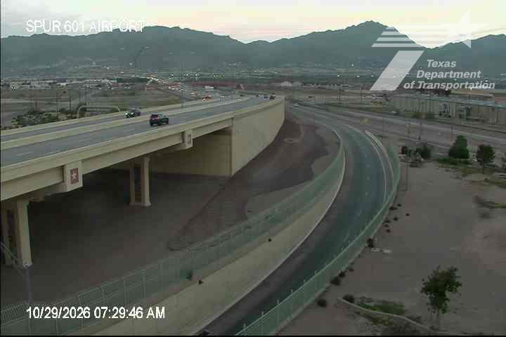 A multi-lane highway with an overpass curves around a construction area, with light traffic moving in both directions under clear skies.