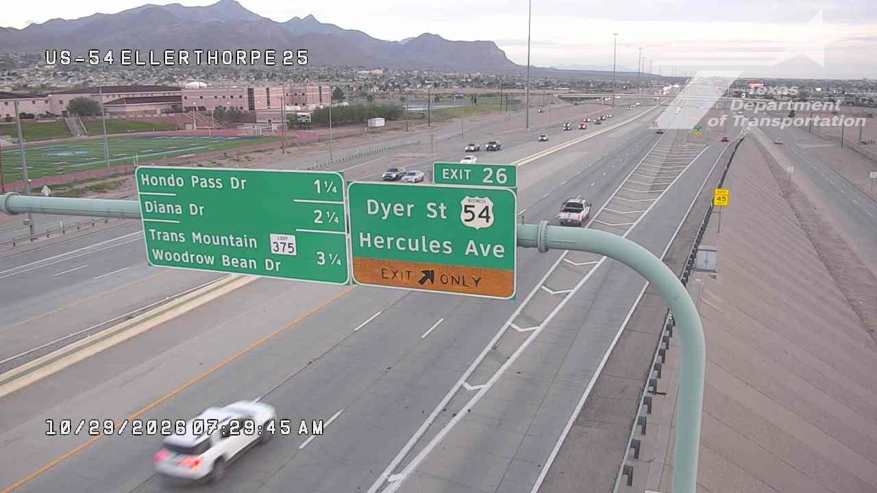 Light traffic flows on a multi-lane highway with clear directional signs for exits to Dyer St and Hercules Ave, under a clear sky with distant mountains in the background.