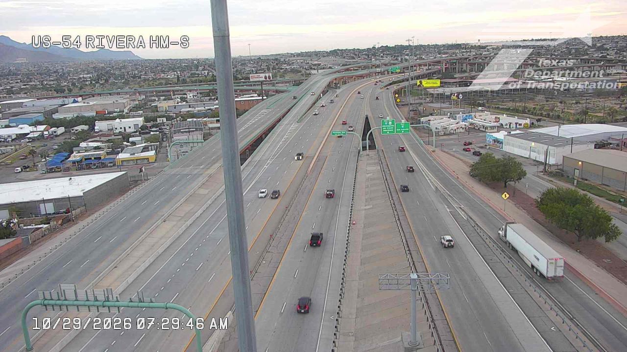 Multi-lane highway with moderate traffic flow, featuring a large overpass and distant mountains under clear skies.