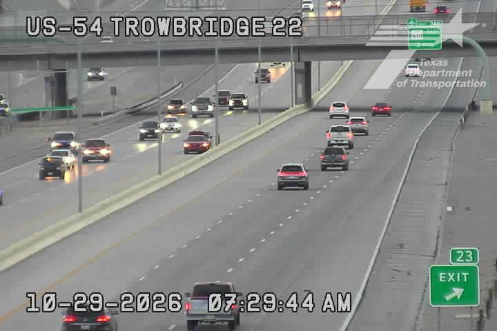 Multi-lane highway with moderate traffic flow under an overpass, vehicles moving in both directions with no visible incidents or road work.
