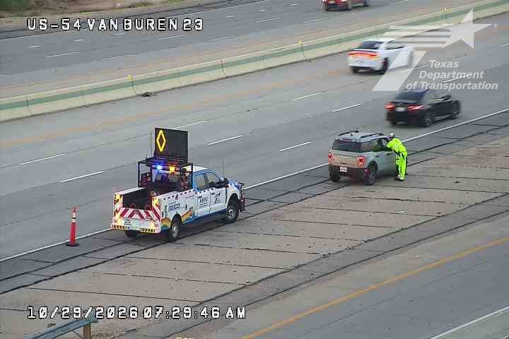 A highway work zone with a utility truck and a worker in high-visibility gear attending to a stopped SUV; traffic flows normally in adjacent lanes.