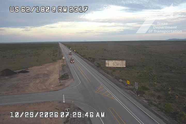 A wide, multi-lane highway stretches through a flat, arid landscape with sparse vegetation under a partly cloudy sky; light traffic moves in both directions with no visible incidents or road work.